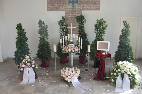 Dekorierte Altarfl&auml;che mit Blumenarrangements, Kerzen und gr&uuml;nen Pflanzen in einer hellen Umgebung.