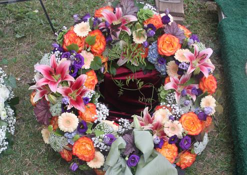 Bunter Kranz aus verschiedenen Blumen, darunter Lilien und Rosen, auf gr&uuml;nem Grass hinterlegt.