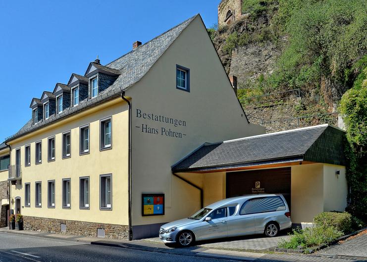 Aktuelle Gebäudeansicht des Bestattungsinstitut mit Bestattungsfahrzeug vor der Garage