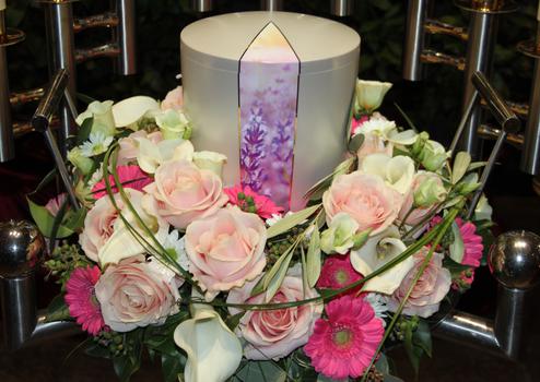 Eine wei&szlig;e Urne mit Urnenkranz mit rosa Rosen, wei&szlig;en Calla und pinken Gerbera.